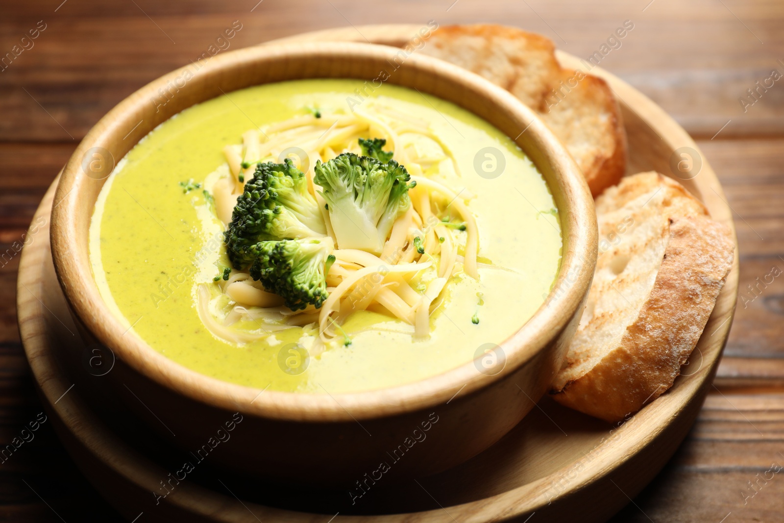 Photo of Delicious broccoli cream soup in bowl and croutons on wooden table, closeup