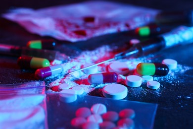 Photo of Drug addiction. Different pills, powder and syringe on dark table in neon lights, closeup