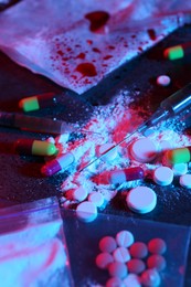 Photo of Drug addiction. Different pills, powder and syringes on dark table in neon lights, closeup