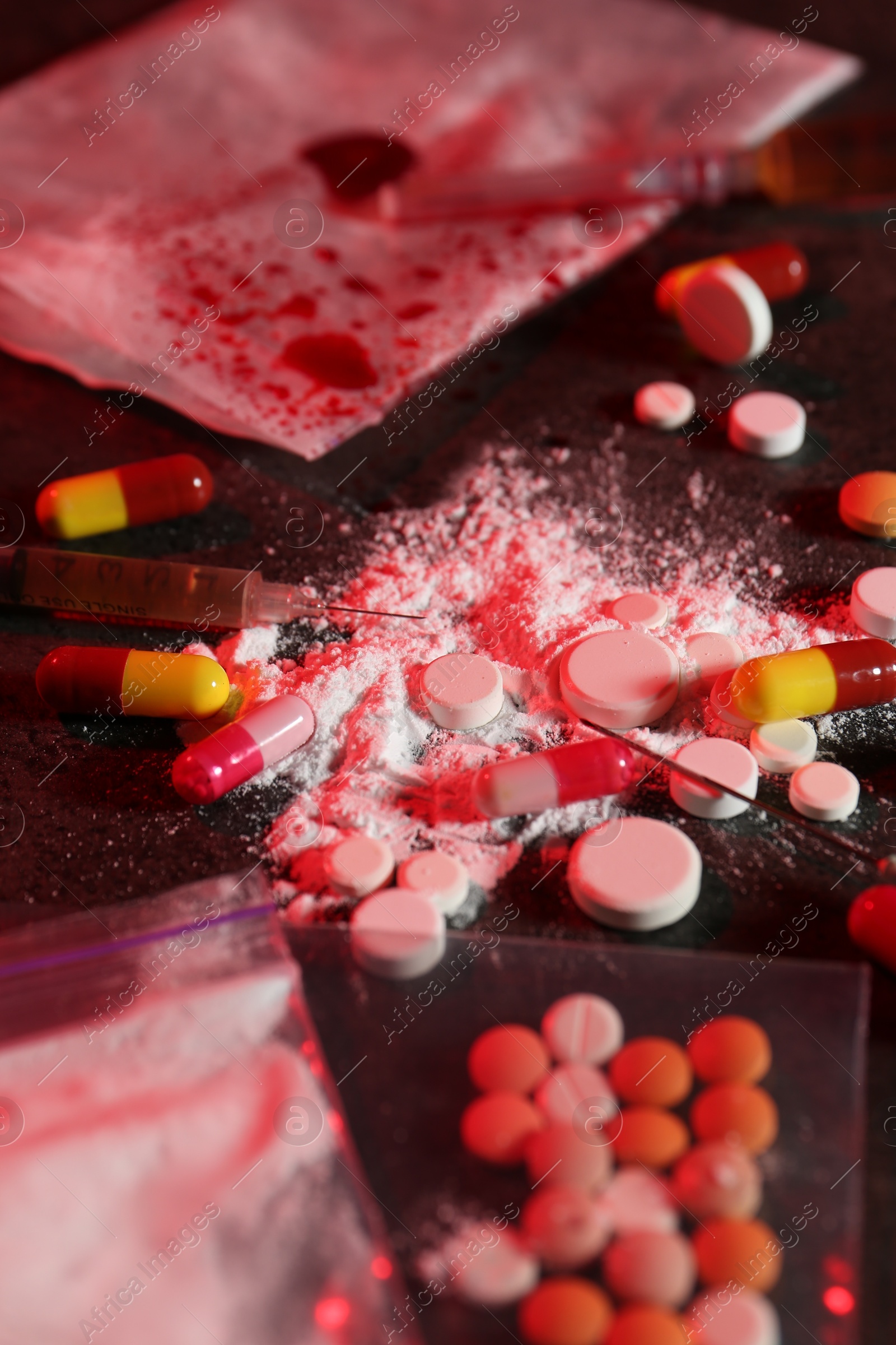 Photo of Drug addiction. Different pills, powder and syringes on dark table in color light, closeup