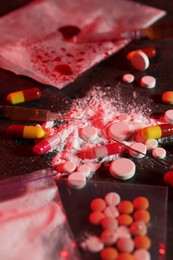 Photo of Drug addiction. Different pills, powder and syringes on dark table in color light, closeup