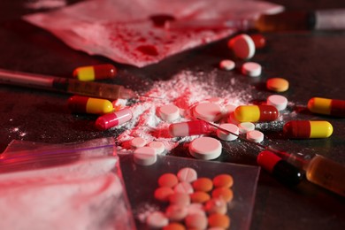 Photo of Drug addiction. Different pills, powder and syringes on dark table in color light, closeup