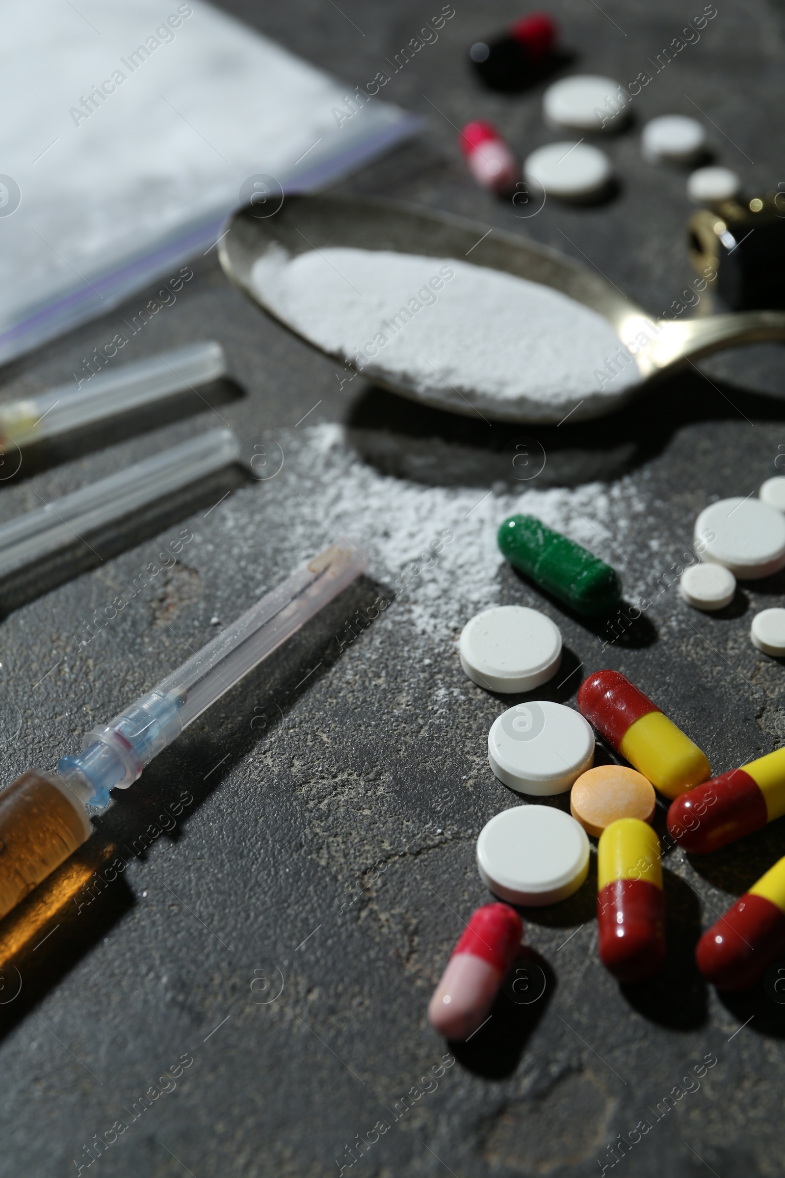 Photo of Drug addiction. Spoon with powder, pills and syringes on gray textured table, closeup