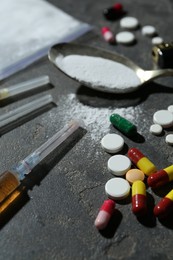 Photo of Drug addiction. Spoon with powder, pills and syringes on gray textured table, closeup