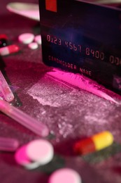 Photo of Drug addiction. Credit card, powder, pills and syringes on dark table in color light, closeup