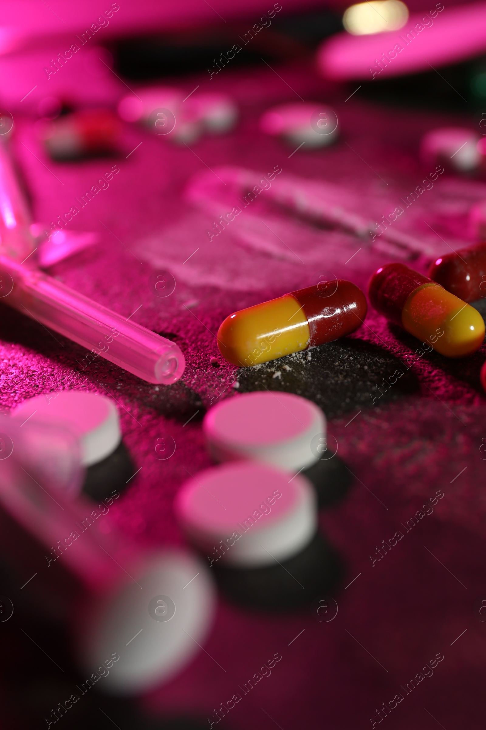 Photo of Drug addiction. Different pills and syringe on table in color light, closeup