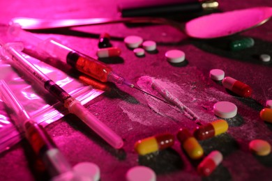 Photo of Drug addiction. Plastic bag with powder, syringes and pills on table in color light, closeup