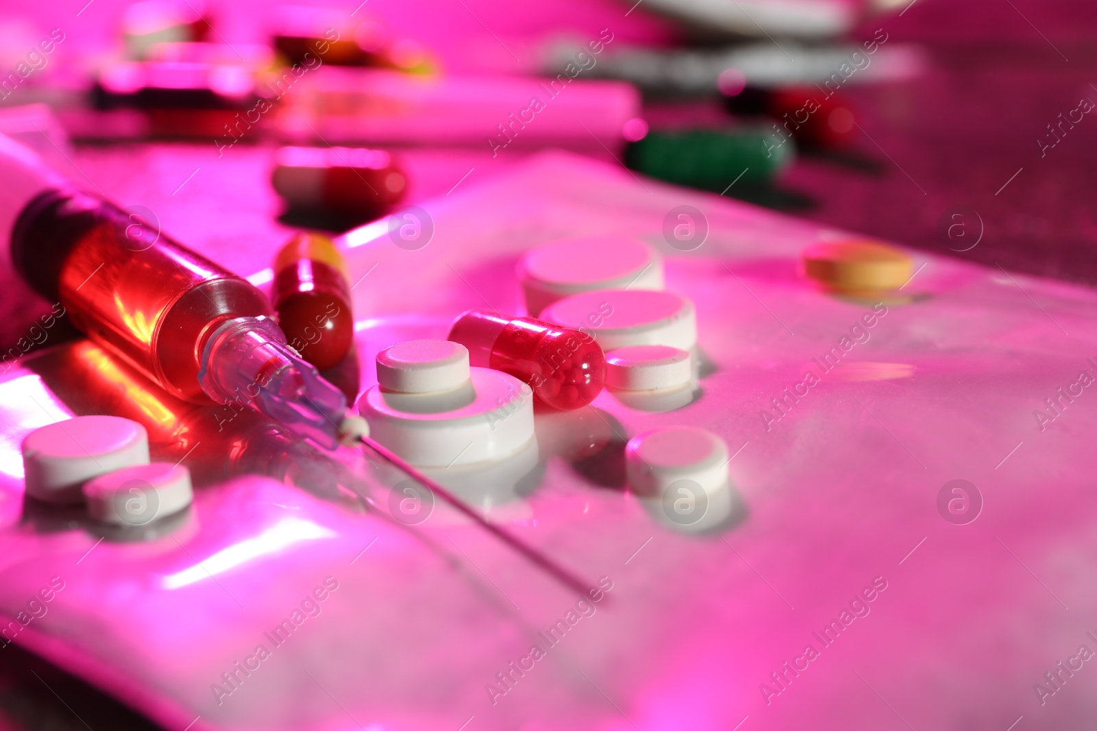 Photo of Drug addiction. Different pills and syringe on table in color light, closeup