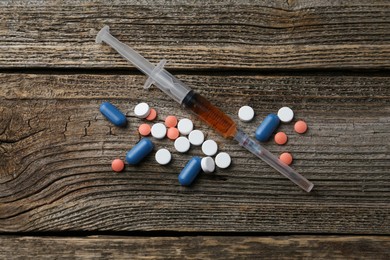 Photo of Drug addiction. Syringe and pills on wooden table, flat lay