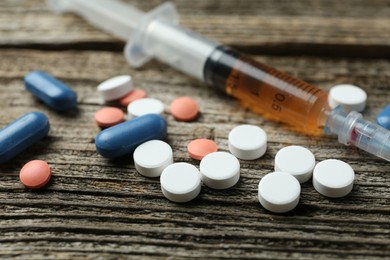 Photo of Drug addiction. Syringe and pills on wooden table, closeup