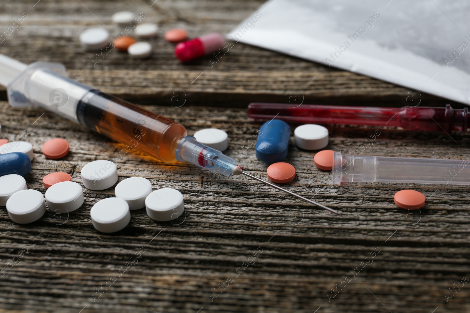 Photo of Drug addiction. Syringes, pills and plastic bag with powder on wooden table, closeup