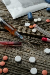 Photo of Drug addiction. Plastic bag with powder, syringes and pills on wooden table, closeup