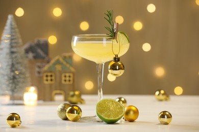 Photo of Tasty Christmas cocktail in glass and decor on white table against dark beige background with blurred lights