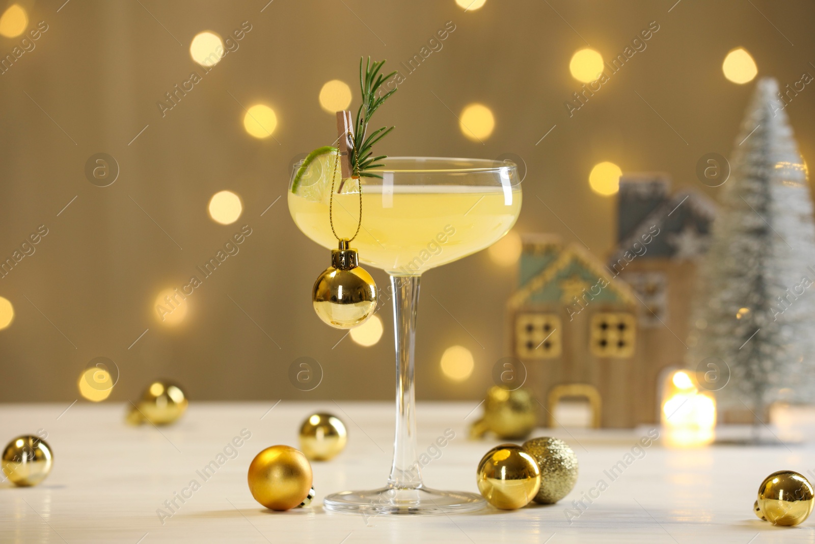 Photo of Tasty Christmas cocktail in glass and decor on white table against dark beige background with blurred lights