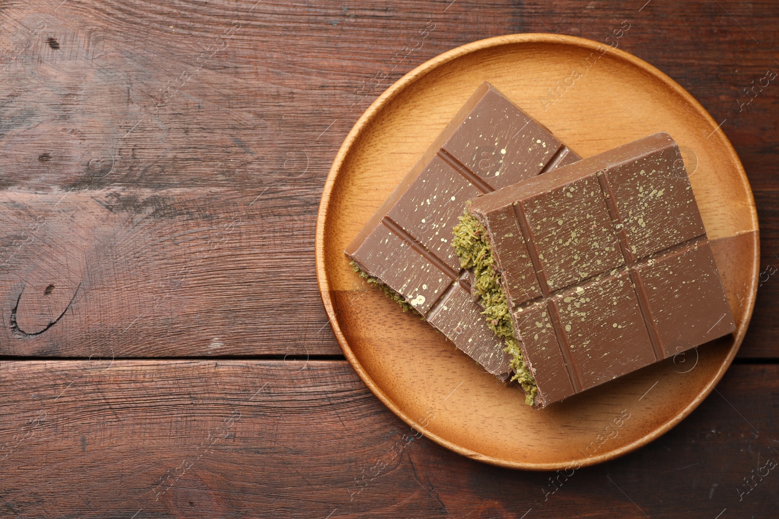 Photo of Pieces of tasty Dubai chocolate with pistachios and knafeh on wooden table, top view. Space for text