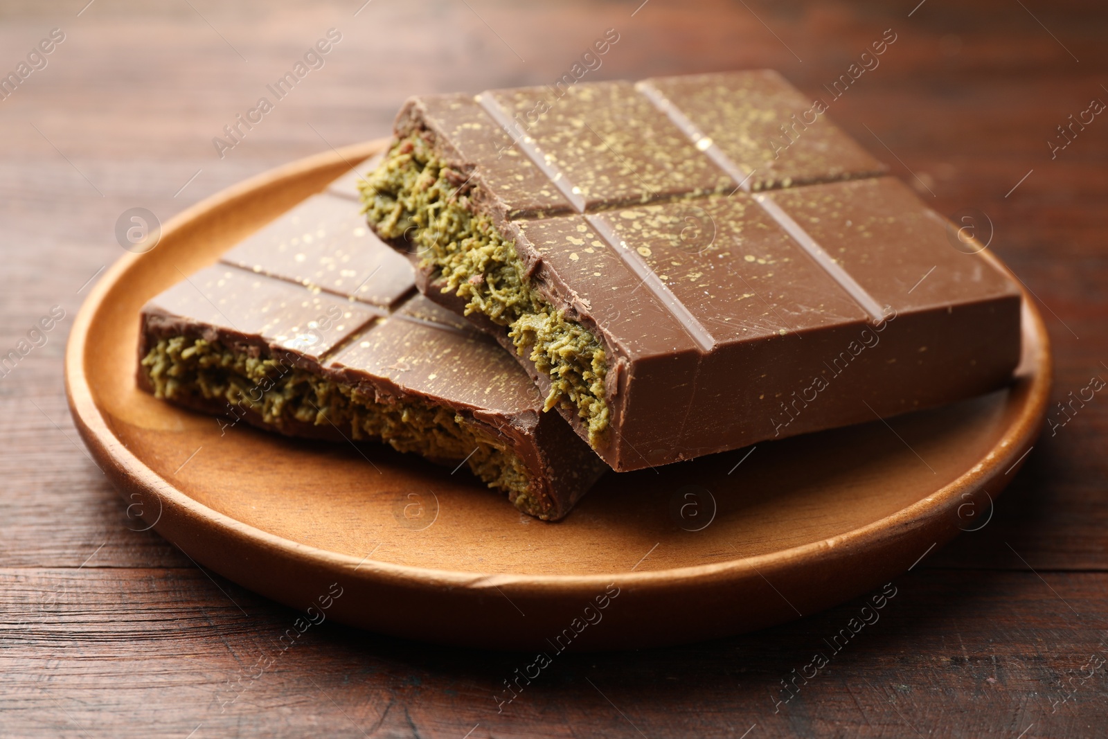 Photo of Pieces of tasty Dubai chocolate with pistachios and knafeh on wooden table, closeup