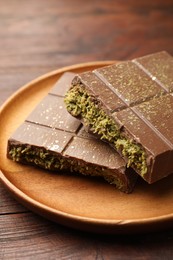 Photo of Pieces of tasty Dubai chocolate with pistachios and knafeh on wooden table, closeup