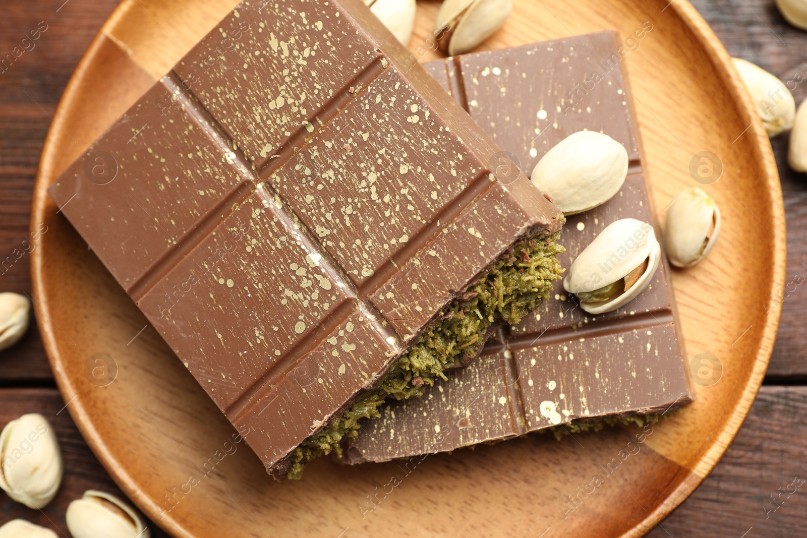 Photo of Pieces of tasty Dubai chocolate with pistachios and knafeh on wooden table, flat lay