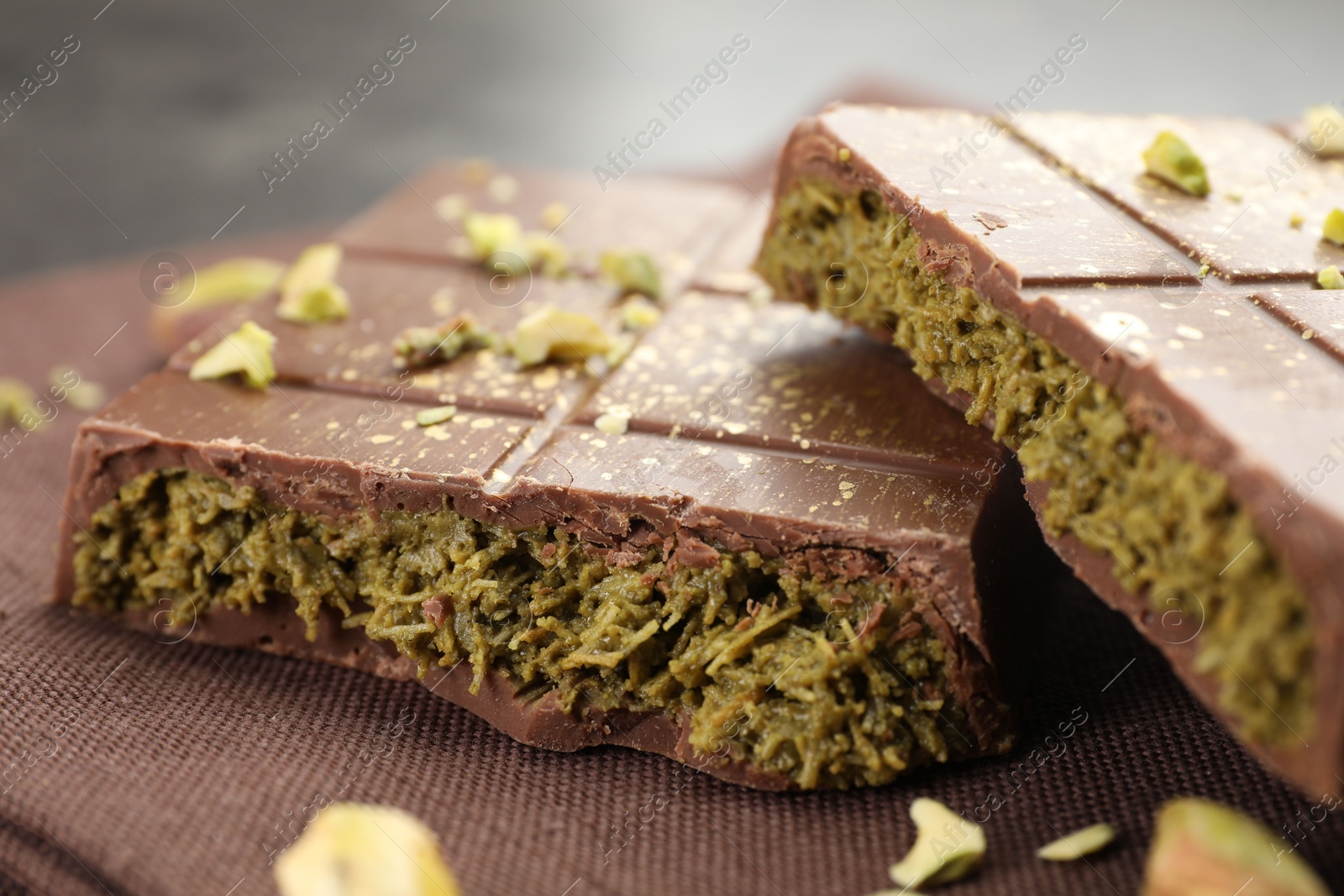 Photo of Pieces of tasty Dubai chocolate bar with pistachios and knafeh on table, closeup