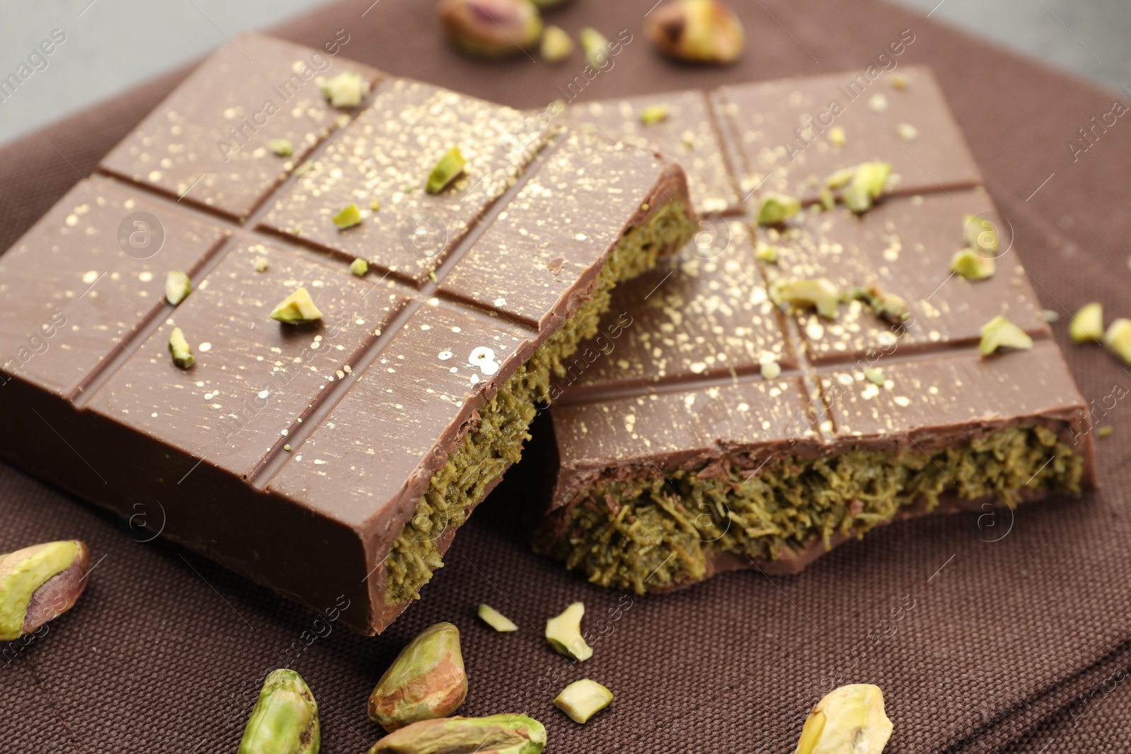 Photo of Pieces of tasty Dubai chocolate bar with pistachios and knafeh on table, closeup