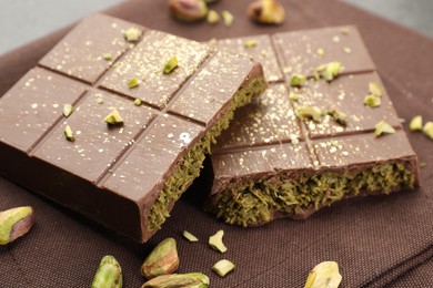 Photo of Pieces of tasty Dubai chocolate bar with pistachios and knafeh on table, closeup