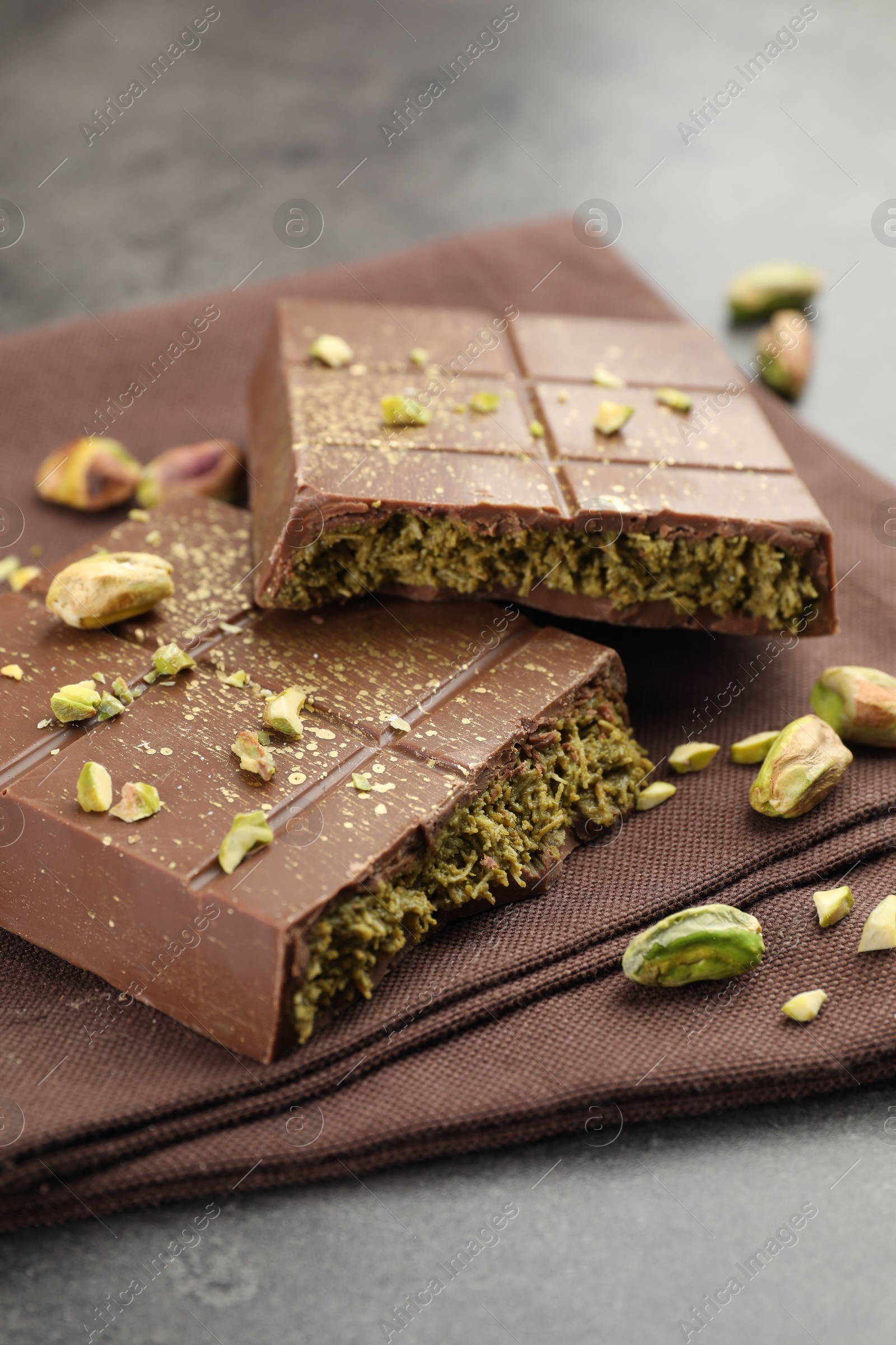 Photo of Pieces of tasty Dubai chocolate with pistachios and knafeh on grey table, closeup