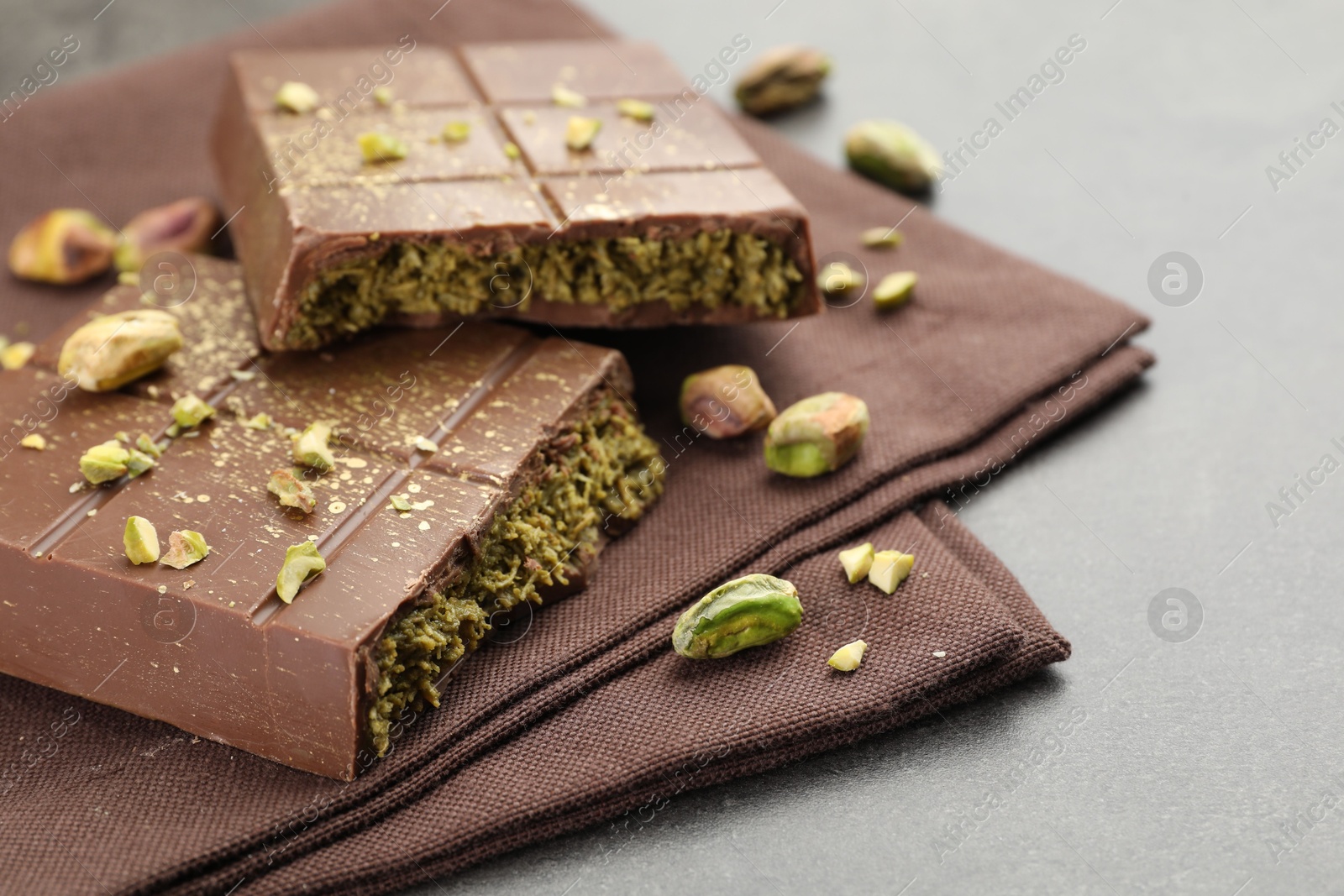 Photo of Pieces of tasty Dubai chocolate with pistachios and knafeh on grey table, closeup