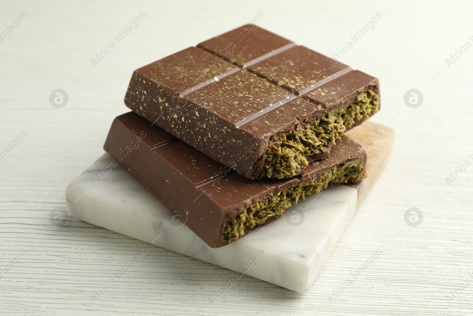 Photo of Pieces of tasty Dubai chocolate with pistachios and knafeh on white wooden table, closeup