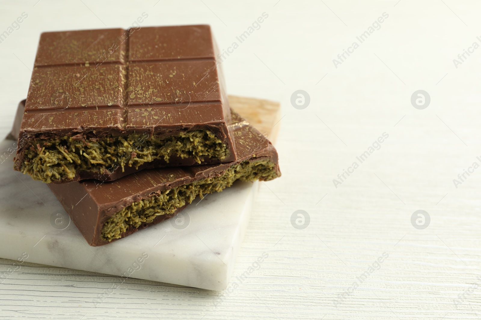 Photo of Pieces of tasty Dubai chocolate with pistachios and knafeh on white wooden table, closeup. Space for text