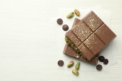 Photo of Pieces of tasty Dubai chocolate with pistachios, knafeh and cacao chips on white wooden table, flat lay. Space for text