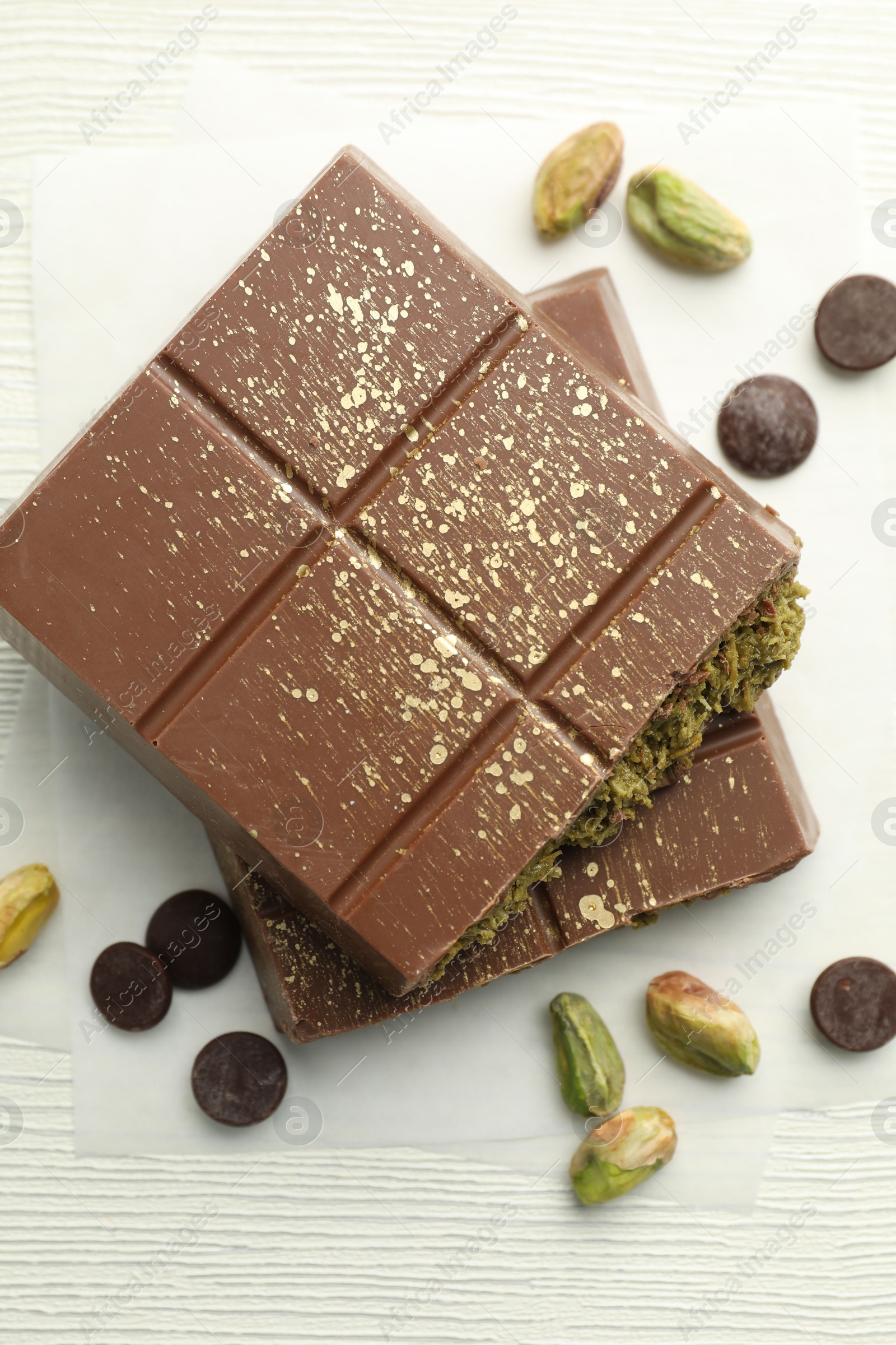 Photo of Pieces of tasty Dubai chocolate with pistachios, knafeh and cacao chips on white wooden table, flat lay