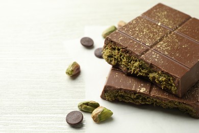 Photo of Pieces of tasty Dubai chocolate with pistachios, knafeh and cacao chips on white wooden table, closeup. Space for text