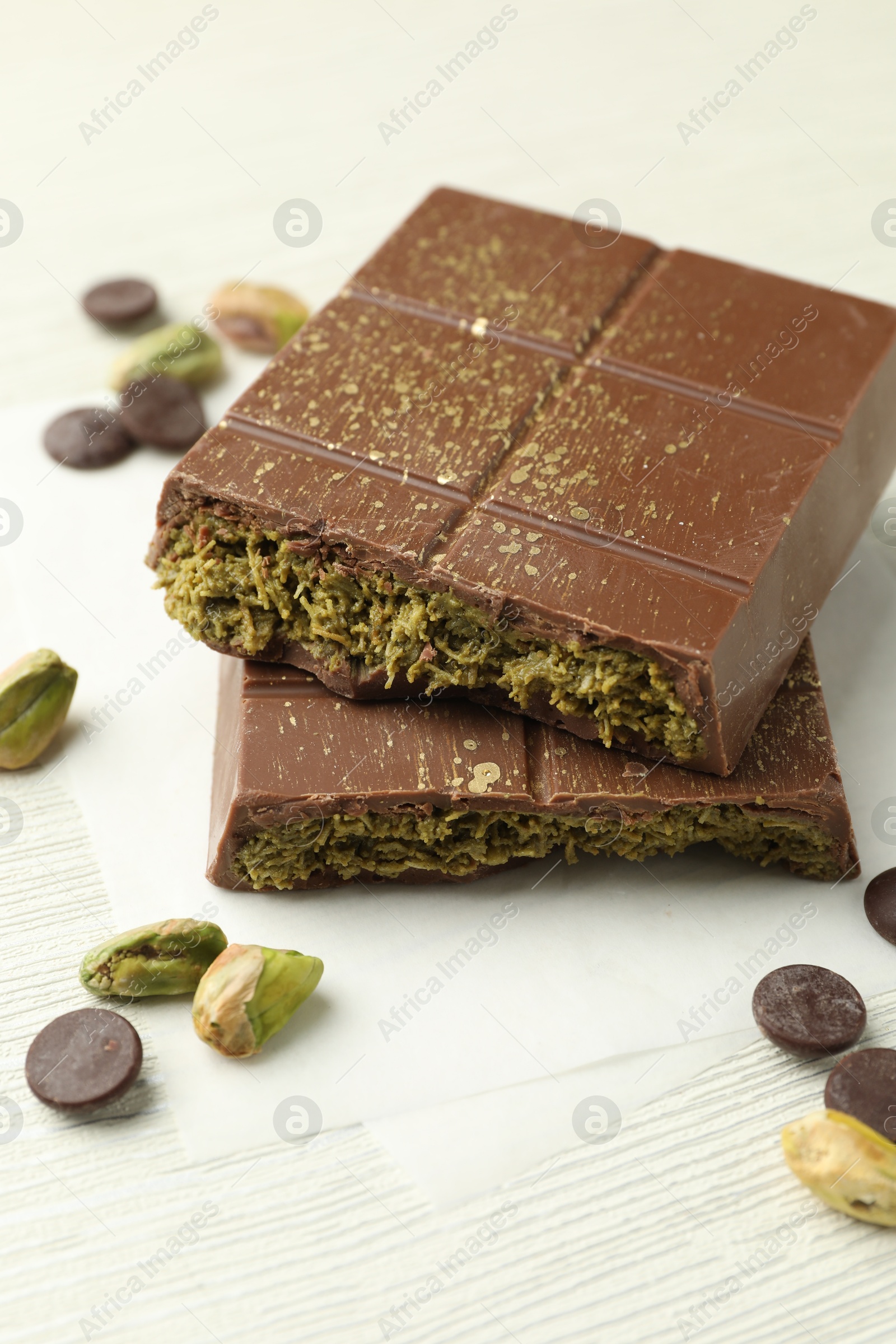 Photo of Pieces of tasty Dubai chocolate with pistachios, knafeh and cacao chips on white wooden table, closeup