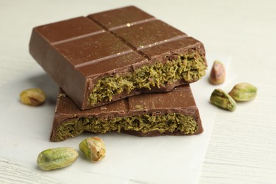 Photo of Pieces of tasty Dubai chocolate with pistachios and knafeh on white wooden table, closeup