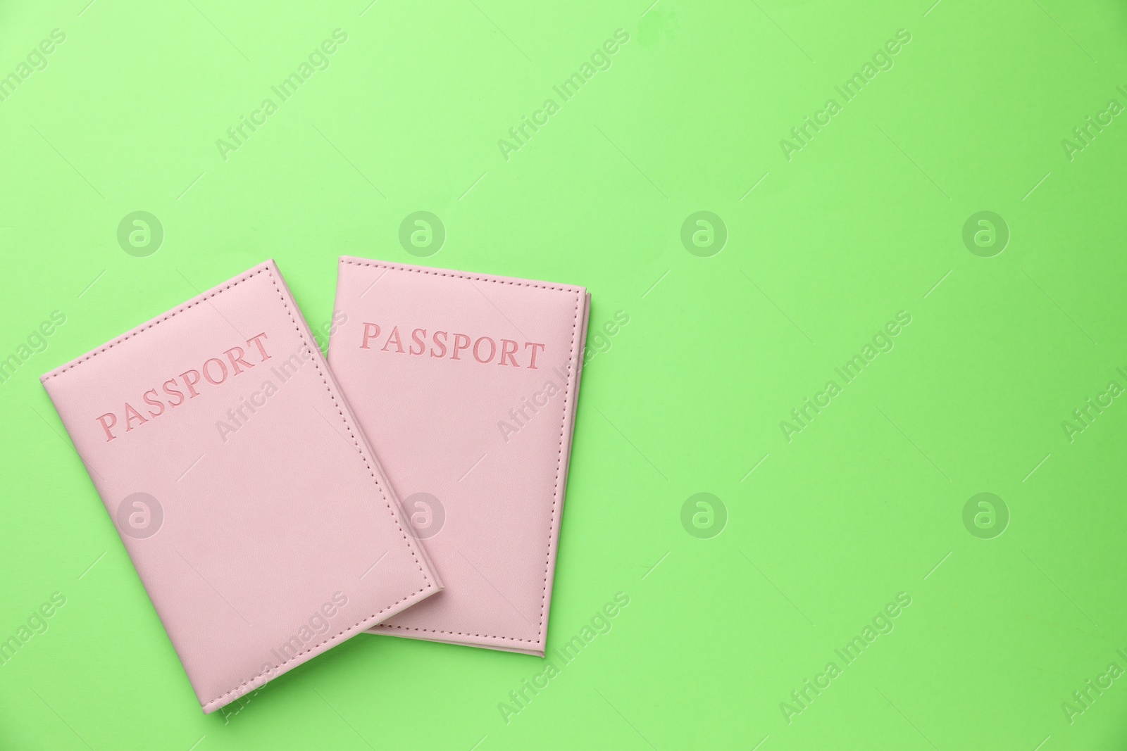 Photo of Passports in pink covers on green background, top view. Space for text