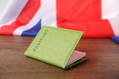 Photo of Passport in green cover and flag of United Kingdom on wooden table, closeup