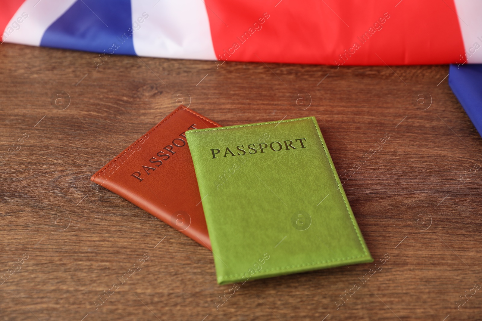 Photo of Passports in color covers and flag of United Kingdom on wooden table, closeup