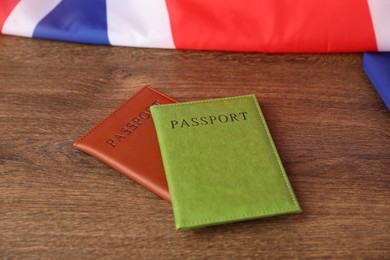 Photo of Passports in color covers and flag of United Kingdom on wooden table, closeup