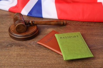 Photo of Passports in color covers, gavel and flag of United Kingdom on wooden table, closeup