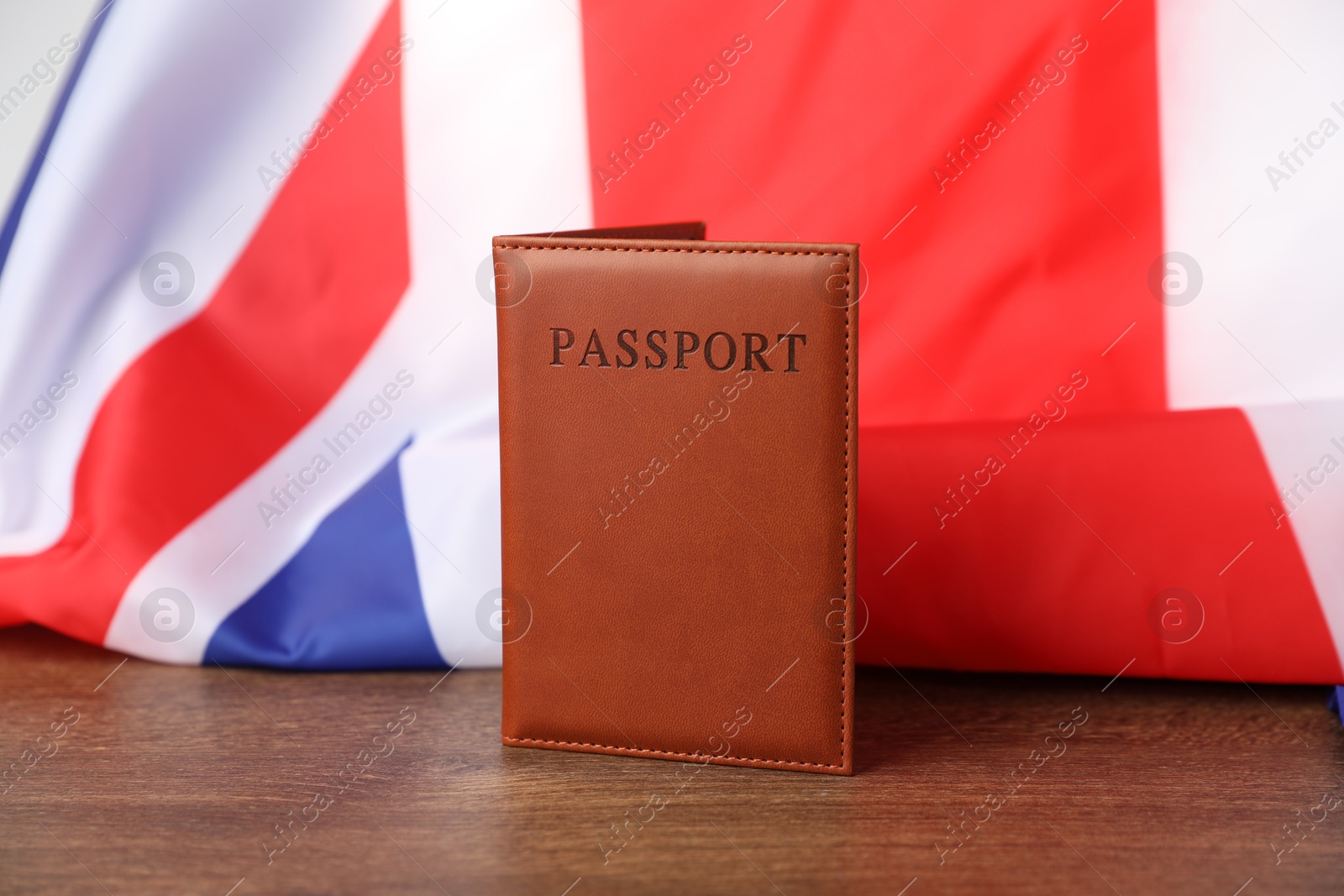 Photo of Passport in brown cover and flag of United Kingdom on wooden table