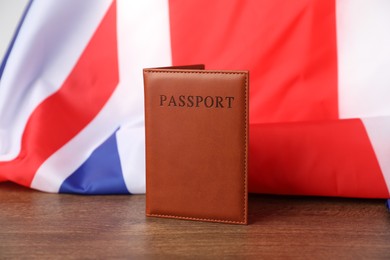 Photo of Passport in brown cover and flag of United Kingdom on wooden table