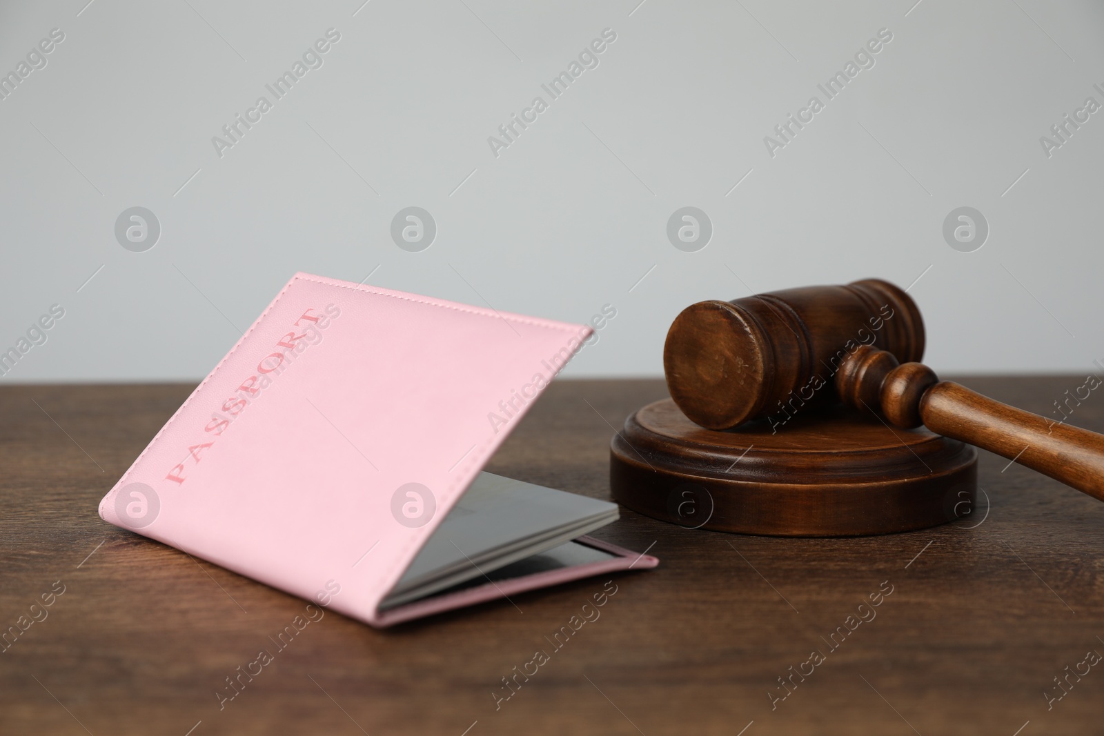 Photo of Passport in pink cover and judge's gavel on wooden table, closeup