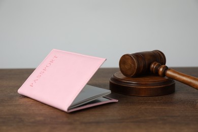 Photo of Passport in pink cover and judge's gavel on wooden table, closeup