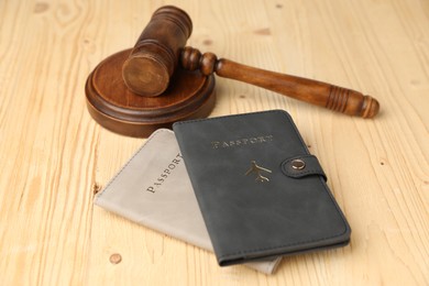 Photo of Passports in color covers and judge's gavel on wooden table, closeup