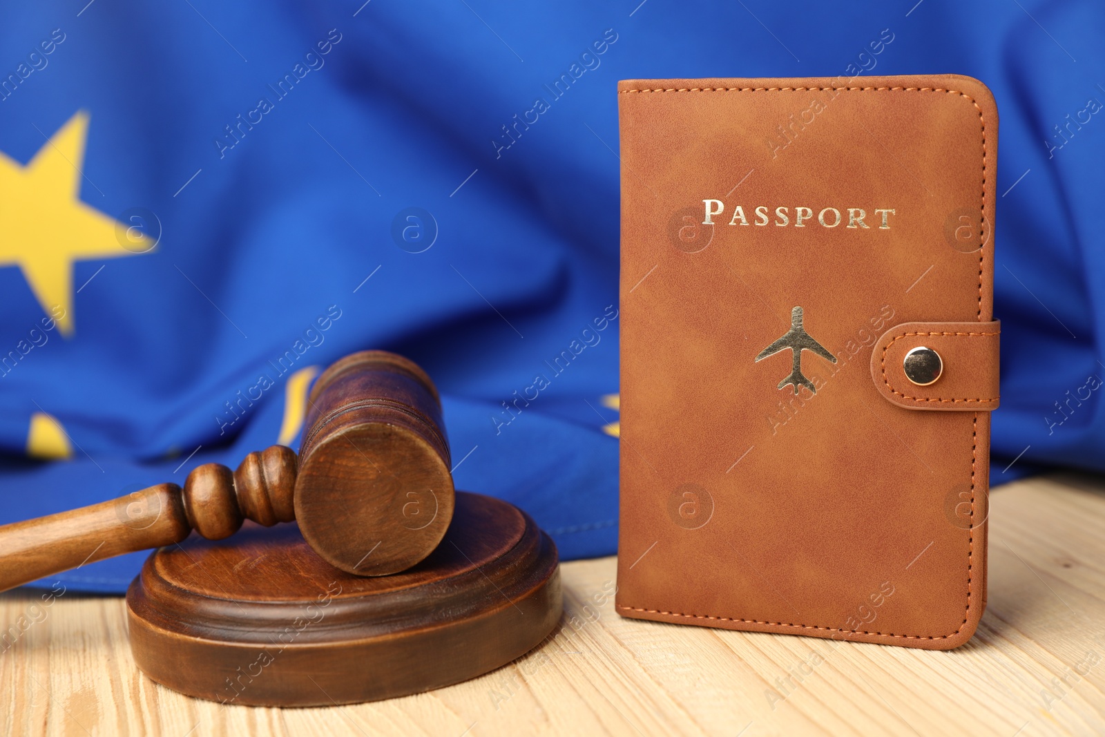 Photo of Passport in brown cover, judge's gavel and flag of European Union on wooden table, closeup