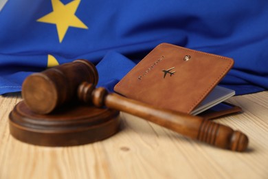 Photo of Passport in brown cover, judge's gavel and flag of European Union on wooden table, closeup