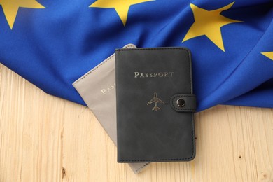 Photo of Passports in leather covers and flag of European Union on wooden table, top view