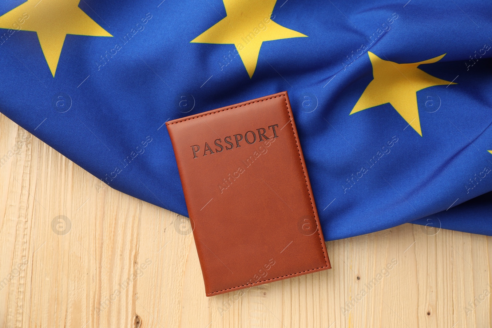 Photo of Passport in brown cover and flag of European Union on wooden table, top view