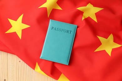 Photo of Passport in light blue cover and flag of China on wooden table, top view