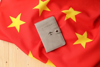 Photo of Passport in leather cover and flag of China on wooden table, top view